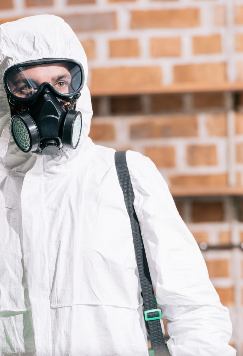 pest control worker standing with sprayer in kitchen and looking away